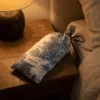 Rest Mode sleep mask in its blue and white patterned storage pouch on a bedside table